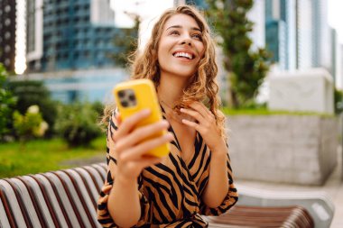 Elinde telefonla gülümseyen bir kadın, metropolün arka planına karşı blog yazıyor ya da video konferans yapıyor. Turistler elinde bir telefonla günbatımı gezintisini severler. Selfie zamanı! Turizm ve blog kavramları.