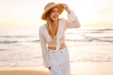 Genç bir kadın gün doğumunda plaj boyunca yürür. Şapkalı neşeli bir kadın açık deniz manzarasını seviyor. Doğa kavramları, rahatlama ve hafta sonları..