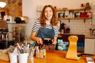Tezgahın arkasında elinde bir fincan taze kahve tutan genç bir bayan barista var. Tecrübeli bir barista rahat bir kafede aromatik kahve hazırlar. İçkiler, konfor ve hazırlık konsepti.
