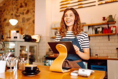 Tezgahın arkasında elinde bir fincan taze kahve tutan genç bir bayan barista var. Tecrübeli bir barista rahat bir kafede aromatik kahve hazırlar. İçkiler, konfor ve hazırlık konsepti.