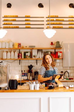 Tezgahın arkasında elinde bir fincan taze kahve tutan genç bir bayan barista var. Tecrübeli bir barista rahat bir kafede aromatik kahve hazırlar. İçkiler, konfor ve hazırlık konsepti.