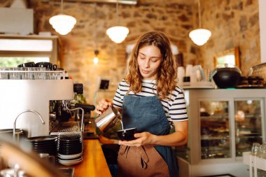 Tezgahın arkasında elinde bir fincan taze kahve tutan genç bir bayan barista var. Tecrübeli bir barista rahat bir kafede aromatik kahve hazırlar. İçkiler, konfor ve hazırlık konsepti.