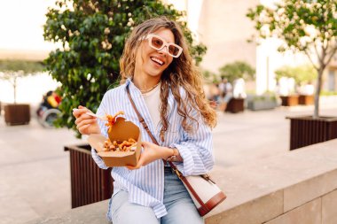 Neşeli bir kadın dışarıda aromatik makarna yer. Güneşli bir günde güzel bir turist bir paket kutusu tutar. Turizm, gıda ve eğlence kavramları.