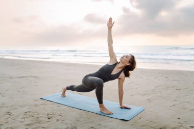Genç bir kadın sabahın köründe plajda minder üzerinde yoga yapıyor. Kadınlar meditasyon yapar, güneşte egzersiz yapar ve deniz manzarasını sever. Kavram rahatlama, egzersiz ve meditasyondur..