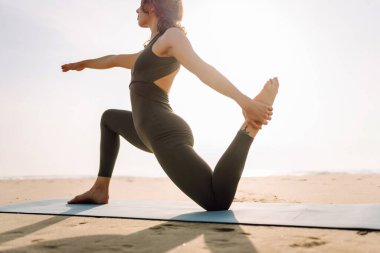 Genç bir kadın sabahın köründe plajda minder üzerinde yoga yapıyor. Kadınlar meditasyon yapar, güneşte egzersiz yapar ve deniz manzarasını sever. Kavram rahatlama, egzersiz ve meditasyondur..