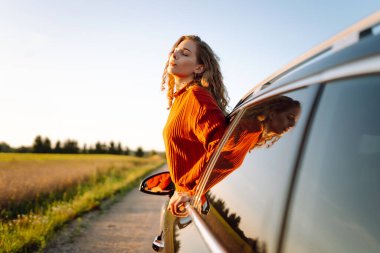 Yolculukta olan güzel bir kadın gün batımında bir arabanın camından sarkmış. Kadın geziyor, kırsal manzaranın tadını çıkarıyor ve güneşli bir günde kendini özgür hissediyor. Ulaşım ve özgürlük kavramı.