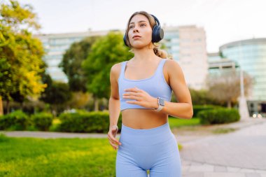Güneşli bir parkta koşan gülümseyen bir kadın. Atletik bir kadın patika boyunca koşar ve güzel havanın tadını çıkarır. Koşmak, spor yapmak ve sağlıklı bir yaşam tarzı..