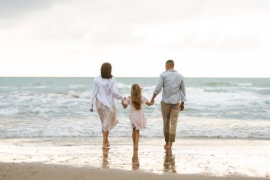 Çocuklu genç bir aile bulutlu bir günde kumlu sahilde geziniyor. Hamile kadın, koca ve çocukları deniz manzarasına hayranlar ve birlikte vakit geçiriyorlar. Aile kavramları, doğa ve yürüyüş..