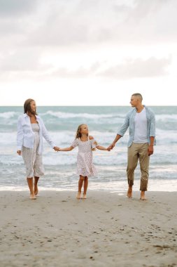 Çocuklu genç bir aile bulutlu bir günde kumlu sahilde geziniyor. Hamile kadın, koca ve çocukları deniz manzarasına hayranlar ve birlikte vakit geçiriyorlar. Aile kavramları, doğa ve yürüyüş..