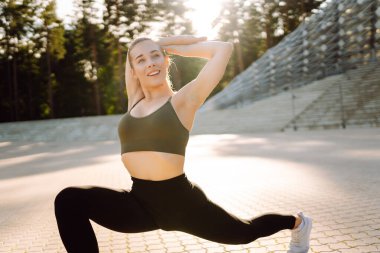 Atletik bir kadın güneşli bir günde spor sahasının merdivenlerinde egzersiz yapar. Genç bir kadın dışarıda antrenman yapıyor. Konsept: Spor, eğitim, açık hava.