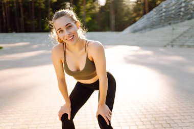 Atletik bir kadın güneşli bir günde spor sahasının merdivenlerinde egzersiz yapar. Genç bir kadın dışarıda antrenman yapıyor. Konsept: Spor, eğitim, açık hava.