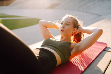 Atletik bir kadın güneşli bir günde spor sahasının merdivenlerinde egzersiz yapar. Genç bir kadın dışarıda antrenman yapıyor. Konsept: Spor, eğitim, açık hava.