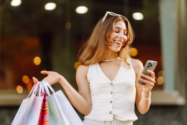 Güneşli bir günde genç bir kadın alışveriş torbaları ve telefonuyla şehirde duruyor. Alışverişten sonra güzel bir kadın, yürüyüşten ve telefonundan mesaj atmaktan zevk alıyor. Tüketim kavramı, alışveriş.