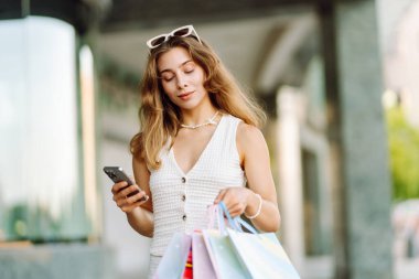 Güneşli bir günde genç bir kadın alışveriş torbaları ve telefonuyla şehirde duruyor. Alışverişten sonra güzel bir kadın, yürüyüşten ve telefonundan mesaj atmaktan zevk alıyor. Tüketim kavramı, alışveriş.