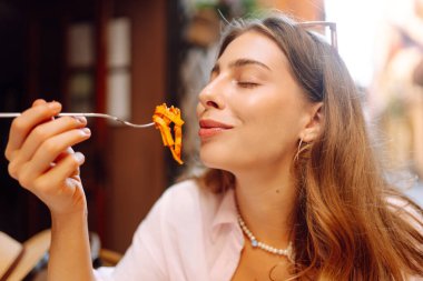 Mutlu bir kadın kafe masasında taze İtalyan makarnası yer. Genç bir turist terasta güneşli bir günde spagetti yiyor. Yemek kavramı, eğlence..