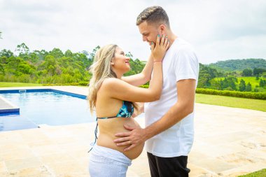 Havuz kenarında genç bir çift. Adam hamile kadının karnını okşuyor..