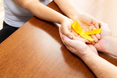 Hands of a couple on the table holding yellow ribbon clipart