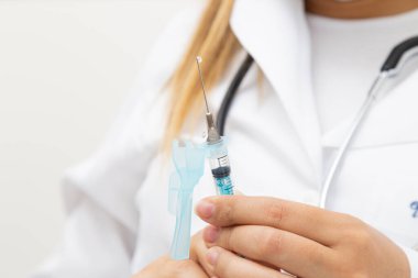 Kadın doktor elinde şırınga ve iğnenin üzerinde bir damla tutuyor..