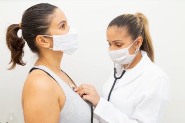 Maskeli doktor maske takan bir hastanın kalbini dinliyor..