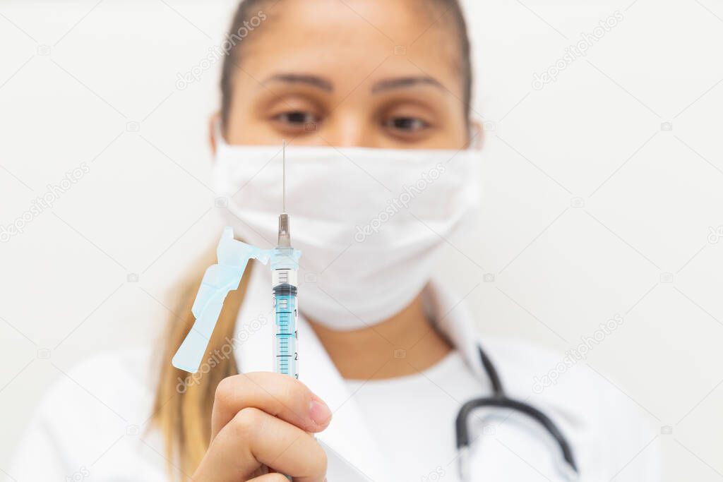 Female doctor staring at the needle of a syringe with vaccine.