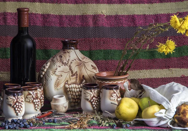 Mesa cubierta con alfombra étnica, vino, jarra de cerámica, vasos, manzanas — Foto de Stock