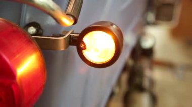 Eski model motosiklet, arka lambaları yanıp sönen bir garajda tamir ediliyor.