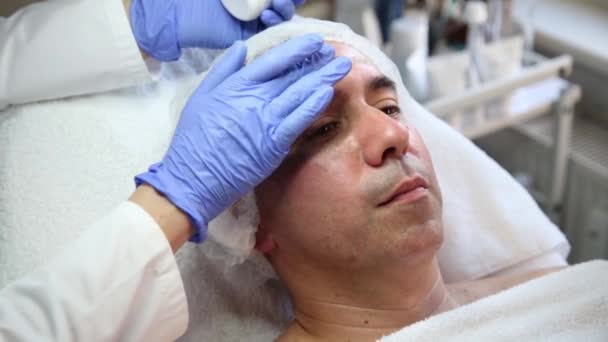 Kosmetyk nakłada krem na twarz człowieka — Wideo stockowe