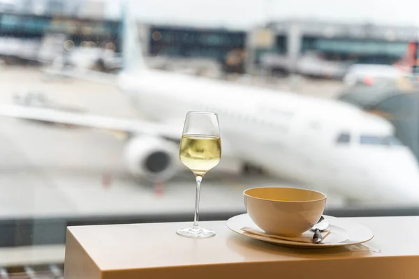 Bir kadeh şarap, pencerenin yanında bir kase çorba ve havaalanı manzaralı bir uçak.