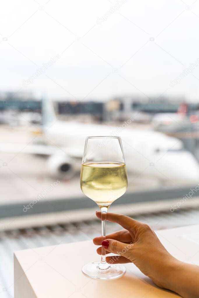 Female hand holding a glass of wine near window with a view to an aircraft