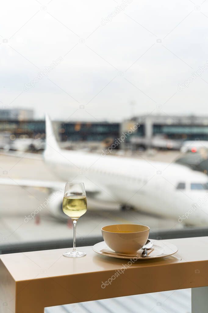 Glass of wine, bowl of soup near window with a view to airplane in airport