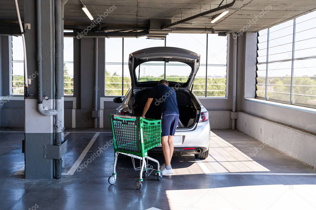 Young man in shirts and t-shirt unloads products from a cart into the car