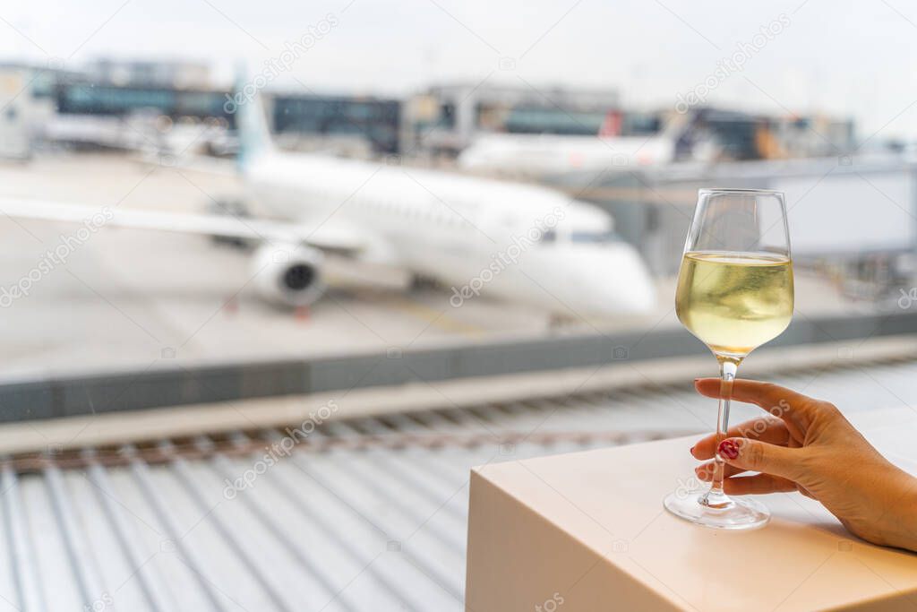 Female hand holding a glass of wine near window with a view to an aircraft