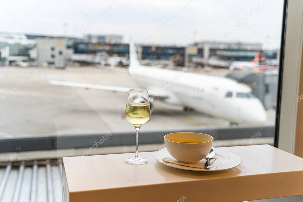 Glass of wine, bowl of soup near window with a view to airplane in airport