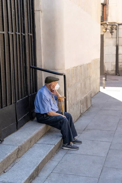 Старик в маске сидит на лестнице в городе в солнечный день — стоковое фото