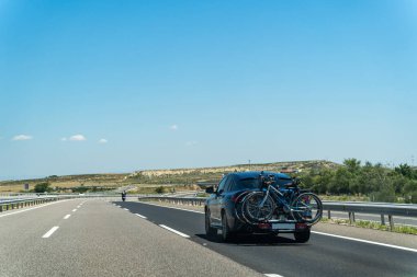 Çöldeki yolda iki bisikleti olan mavi gökyüzü ve çalıları olan bir araba.