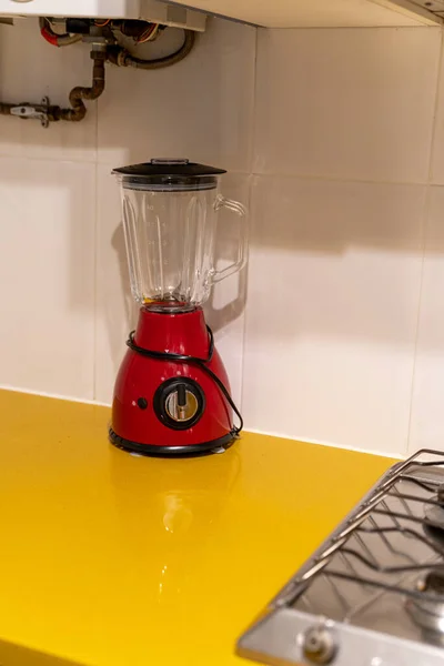 Red electronic mixer stands on a yellow table near the stove in the kitchen