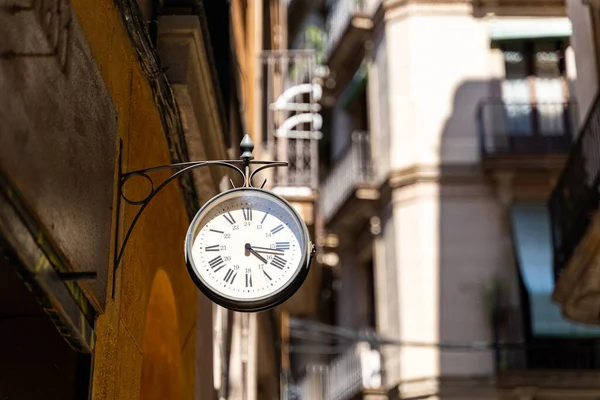 Reloj de calle con flechas en la pared con fondo de edificios en Barcelona —  Fotos de Stock