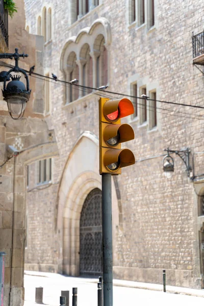 Yellow traffic light showing red on street with medieval buildings in Barcelona