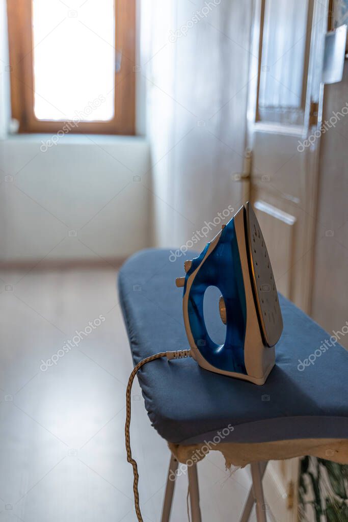 Modern electric iron on board by the door and bright window with daylight