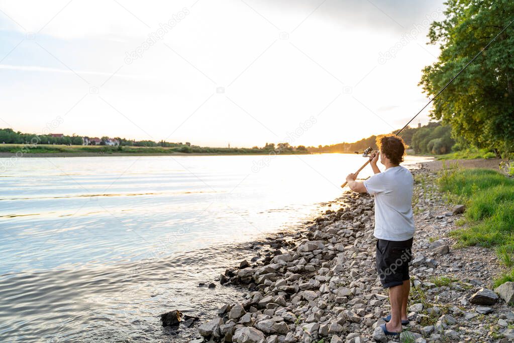 Hands of a fisherman are holding fishing rod with reel on the stony river ridge