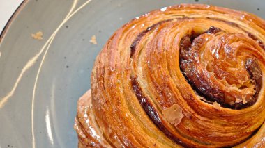 Close-up of a golden brown cinnamon roll with a glossy glaze on a ceramic plate. Concept of sweet bakery pastry, cozy breakfast, and indulgent dessert treat