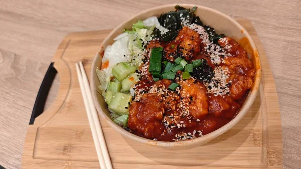 Baharatlı tavuk, taze sebze ve tahtadan tepside sunulan susam tohumlarıyla Kore pirinç kasesi. Görüntü Asya mutfağını, dengeyi ve ev yapımı lezzetli yemek sanatını temsil ediyor.