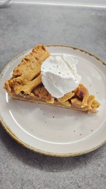 Seramik tabakta servis edilen kremalı ev yapımı elmalı turta. Görüntü sıcak tatlı anlarını, ev yapımı pişirmeyi ve klasik konforlu yemekleri temsil ediyor.