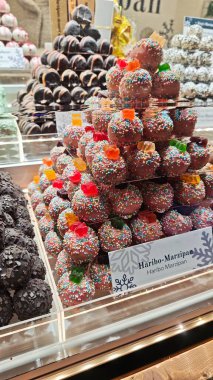 Bu şenlikli gösteride, Haribo-Marzipan piramidi bir Noel pazarında ziyafet veriyor. Her tatlı yuvarlak bir badem ezmesi topudur, pembe çikolataya batırılmış, renkli serpintilerle kaplı.