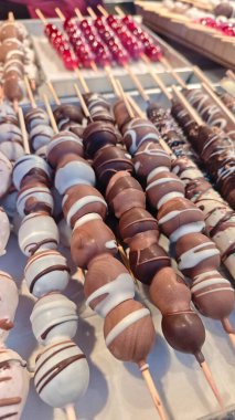 Çikolata kaplı meyveler ahşap çubuklarda şekerleme tezgahında ya da gıda pazarında sergileniyor. Görüntü tatlı, sokak yemeği ve hoşgörü konseptini temsil ediyor.