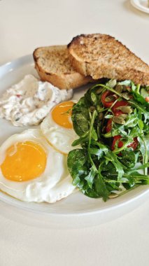 Sağlıklı kahvaltı, kızarmış yumurta, tost, sebze salatası ve krema beyaz tabakta. Sabah yemeği konsepti beslenme, denge ve taze yaşam tarzını sembolize eder.