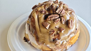 Karamelli fındıklı tarçınlı rulo, beyaz tabakta kremayla yakın çekim. Tatlı tatlı pasta hoşgörü, pastane ziyafeti ve konforlu yiyecek konseptini simgeler.