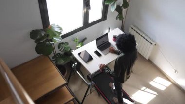 Dizüstü bilgisayarı, telefonu, kulaklığı ve tableti olan genç Afro-Amerikan bir adam küçük bir koşu bandında yürüyordu.