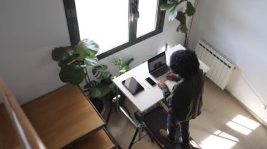 Dizüstü bilgisayarı, telefonu, kulaklığı ve tableti olan genç Afro-Amerikan bir adam küçük bir koşu bandında yürüyordu.