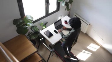 Dizüstü bilgisayarı, telefonu, kulaklığı ve tableti olan genç Afro-Amerikan bir adam küçük bir koşu bandında yürüyordu.